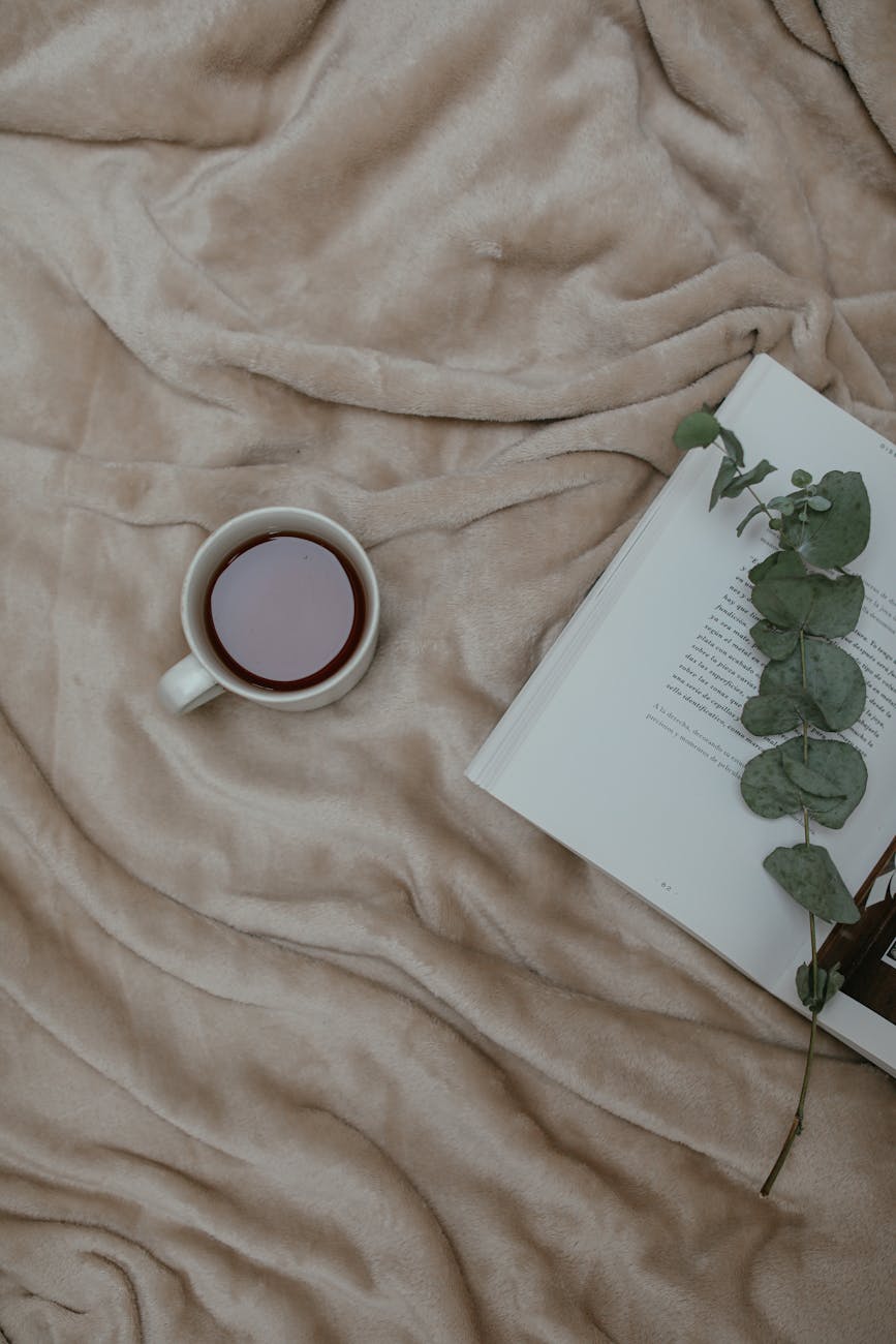a cup of tea beside an open book with stem of green leaves
